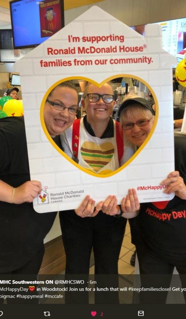 A group of three McDonald's employees posing inside a custom Ronald McDonald House cutout frame.
