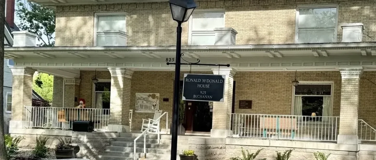 The exterior of the Ronald McDonald House of Northeast Kansas, featuring a large multi-story home with a covered front porch surrounded by green trees.